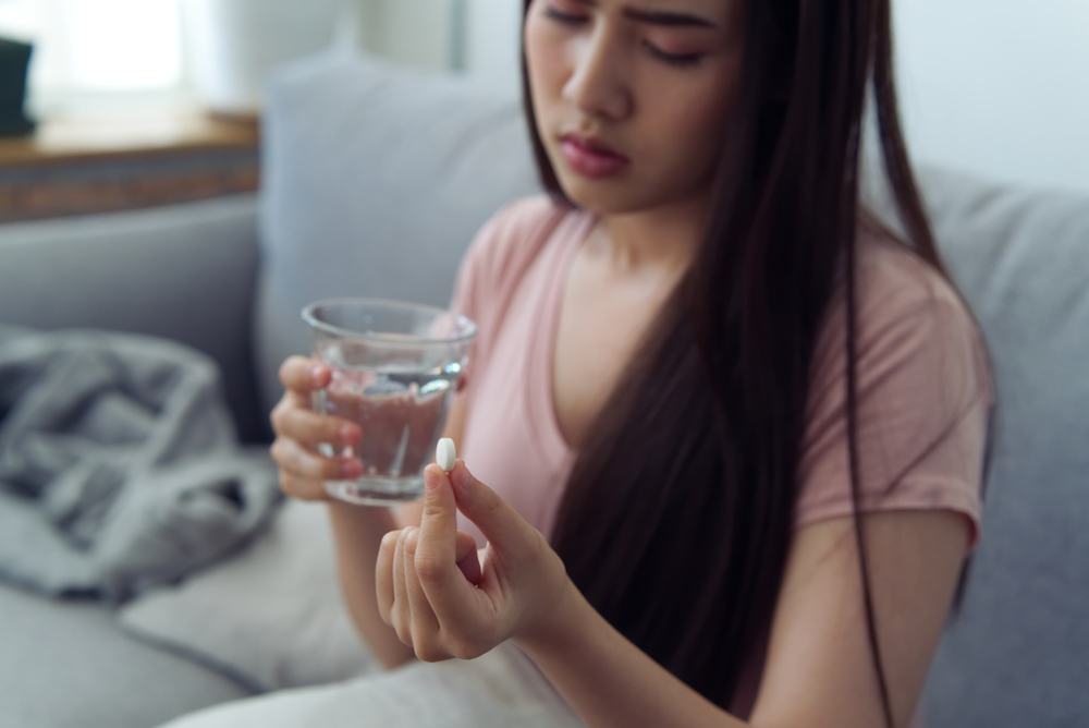Woman looking at pill with glass of water in other hand
